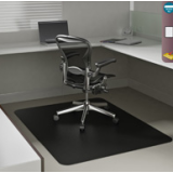 Solid black vinyl desk chair mat covering a worn office floor beneath a rolling chair