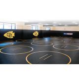 Black roll up wrestling mats with printed circles and team logos in a school wrestling room